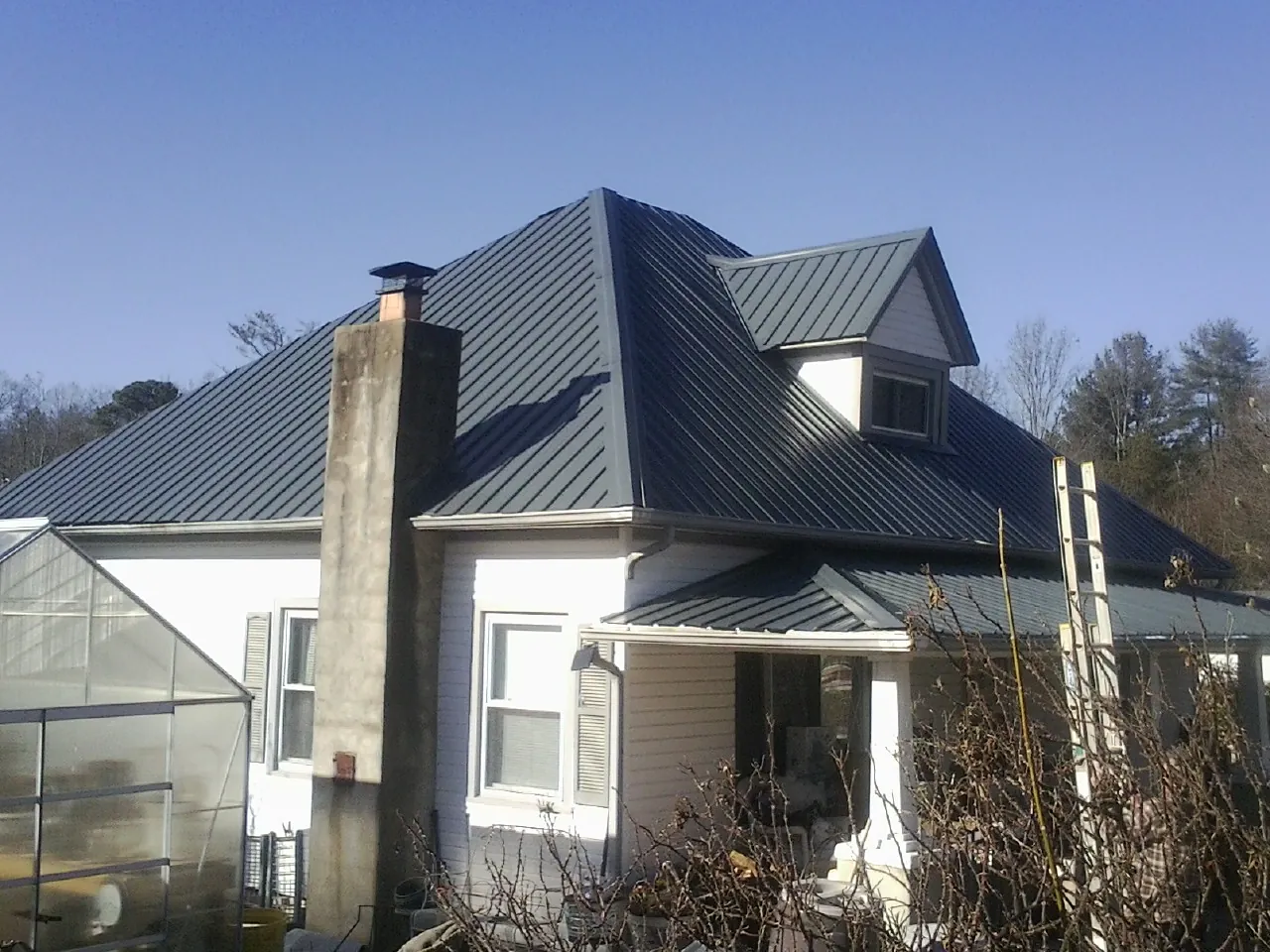 Dark blue standing seam metal roof on a white farmhouse with dormer — Slate & Tile Roof Repair by Roofing Brothers in Stockdale