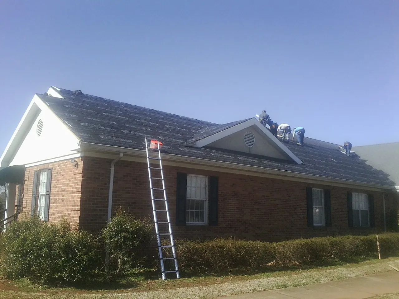Crew tearing shingles off a brick ranch roof with a ladder set — Emergency Roof Repair work by our crew in Stockdale