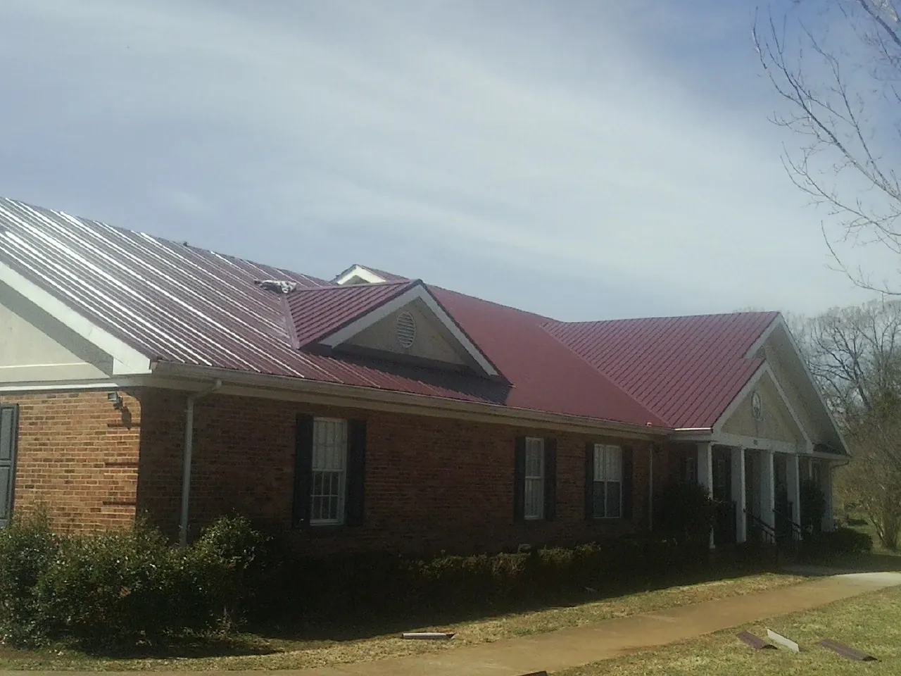 Red metal roof with gabled entries on a long brick building, from a Hail Damage Roof Repair job in Stockdale