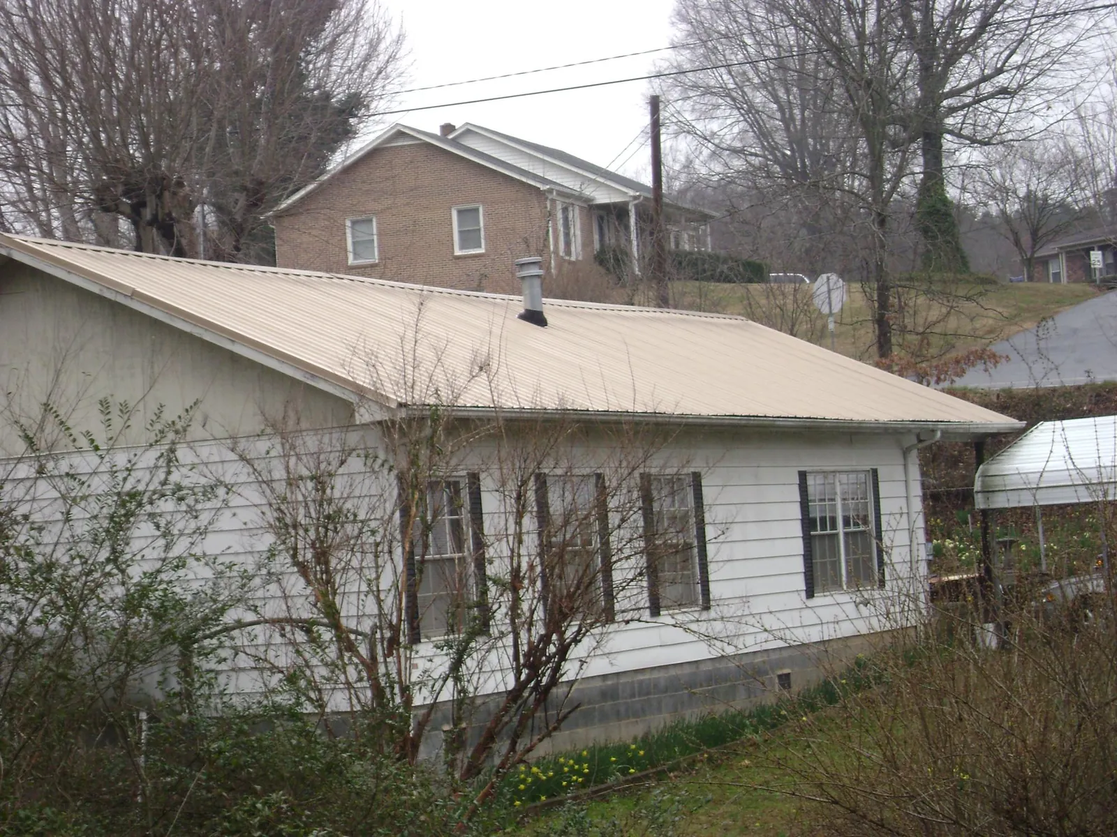 Tan metal roof on a white sided house set into a hillside — Commercial Roofing by Roofing Brothers in Stockdale